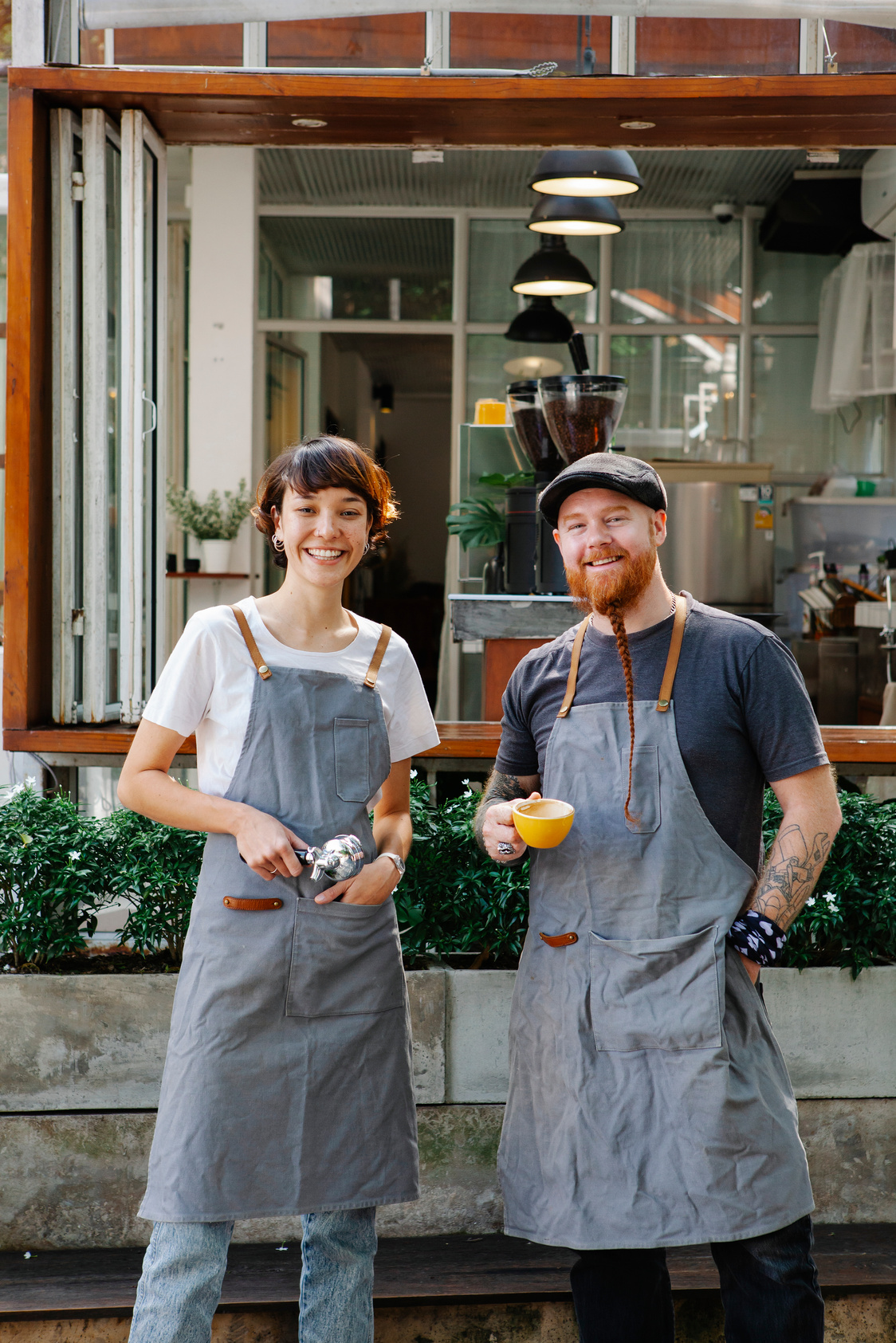 Cheerful baristas in aprons standing near coffee house